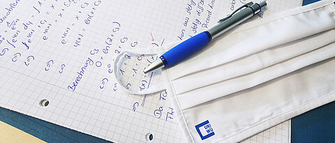 Mund- und Nasenschutz liegt mit Kugelschreiber auf einem Prüfungsblatt