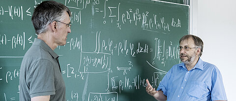 Professors discussing in front of a blackboard